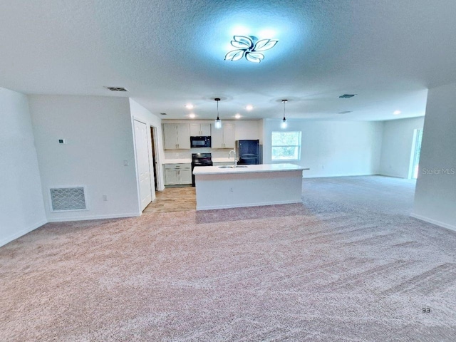 kitchen with visible vents, open floor plan, light carpet, black appliances, and a sink