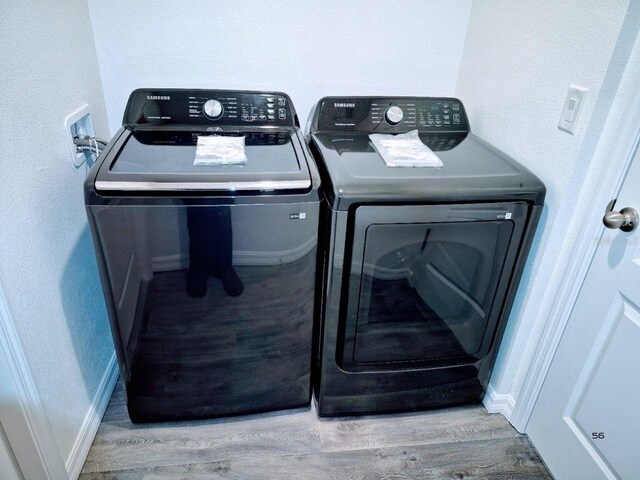 washroom featuring baseboards, wood finished floors, washing machine and dryer, and laundry area