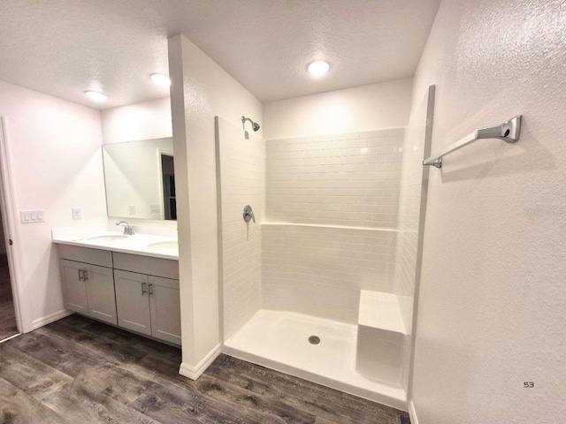 bathroom with tiled shower, a textured ceiling, wood finished floors, and a sink