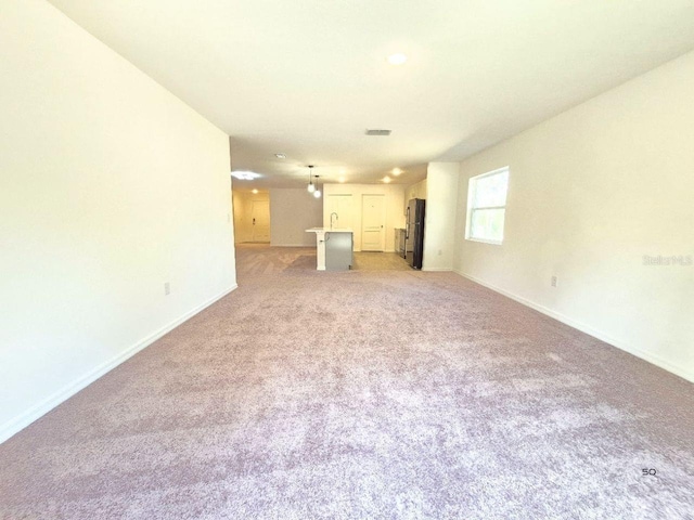 unfurnished living room with light colored carpet, visible vents, and baseboards