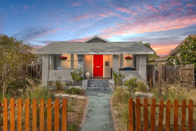 bungalow with covered porch, fence private yard, roof with shingles, and stucco siding