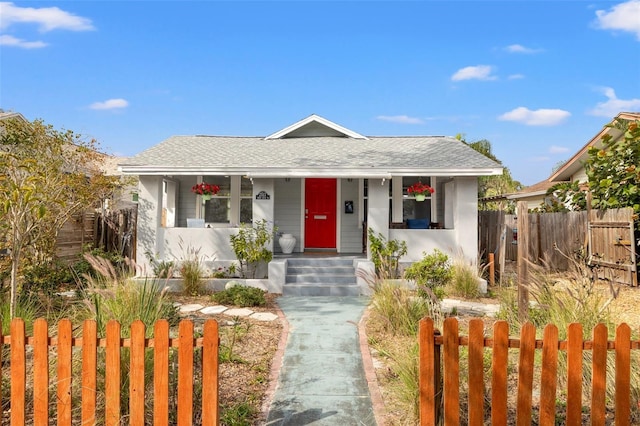 bungalow with a fenced front yard, covered porch, and a shingled roof