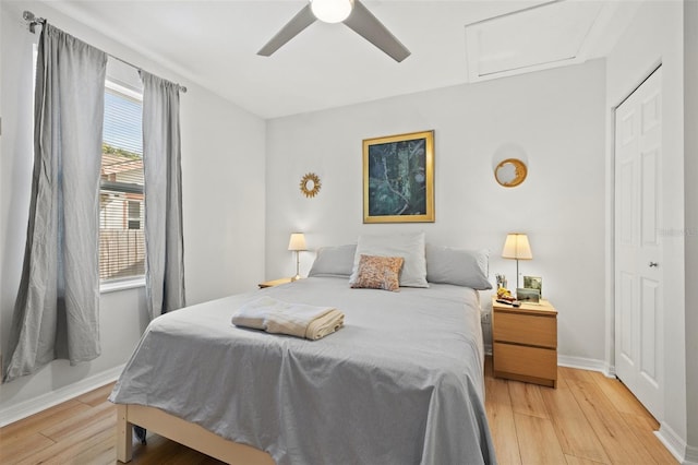 bedroom featuring light wood finished floors, attic access, baseboards, and a ceiling fan