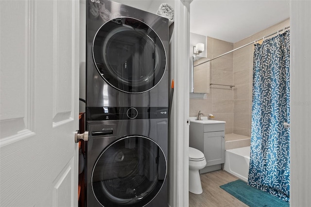 full bath featuring toilet, stacked washer and dryer, wood finished floors, vanity, and shower / bathtub combination with curtain