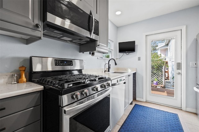 kitchen with baseboards, light tile patterned floors, gray cabinets, appliances with stainless steel finishes, and a sink