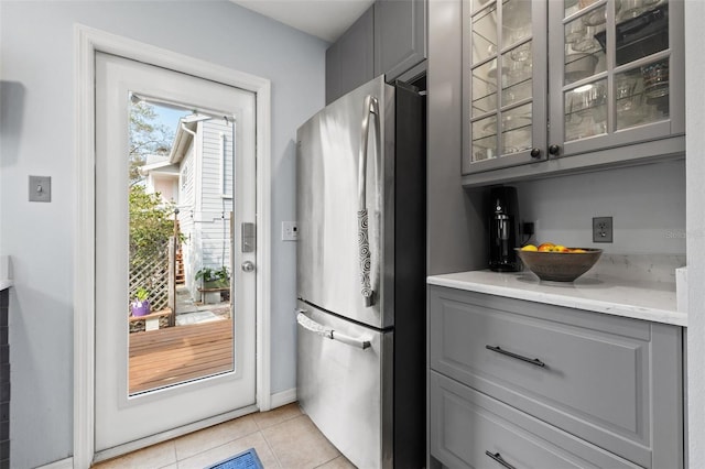 kitchen with light tile patterned flooring, glass insert cabinets, gray cabinets, and freestanding refrigerator