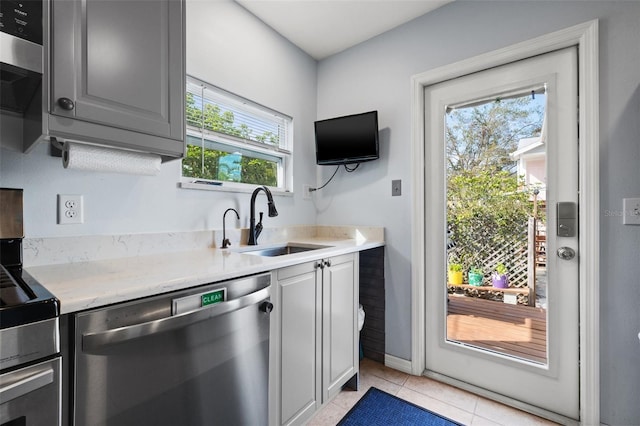 kitchen with light tile patterned floors, gray cabinetry, a sink, light countertops, and stainless steel dishwasher