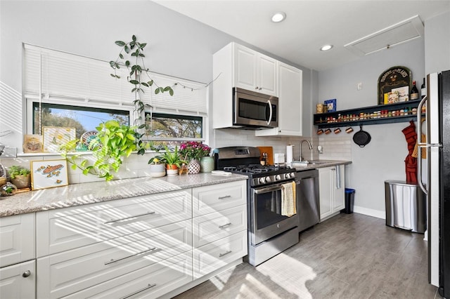 kitchen with a sink, tasteful backsplash, light wood-style floors, appliances with stainless steel finishes, and white cabinets