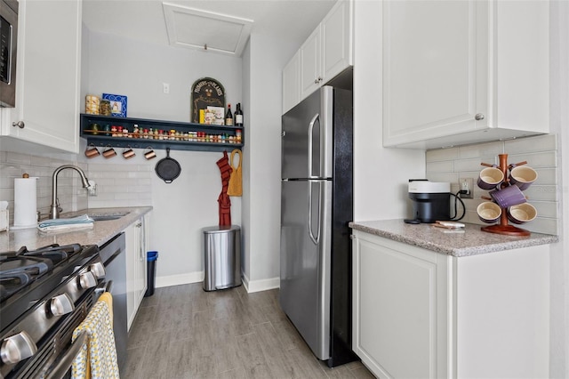 kitchen featuring freestanding refrigerator, a sink, light wood-style floors, white cabinetry, and backsplash