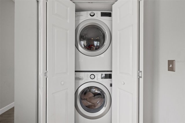 laundry room with baseboards, stacked washer and clothes dryer, wood finished floors, and laundry area