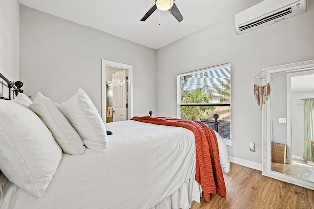 bedroom featuring a wall mounted air conditioner, ensuite bathroom, a ceiling fan, light wood finished floors, and baseboards