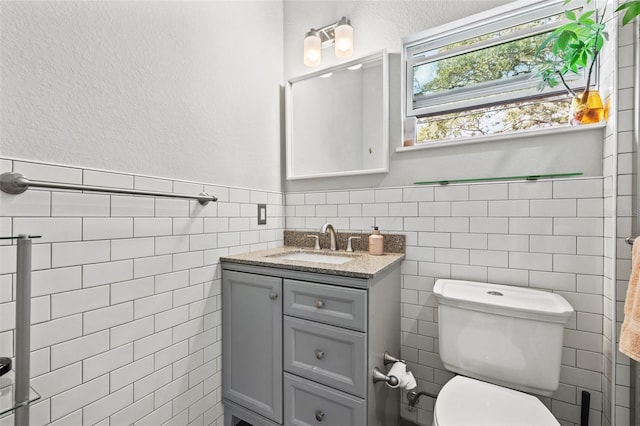 bathroom featuring vanity, tile walls, toilet, and wainscoting