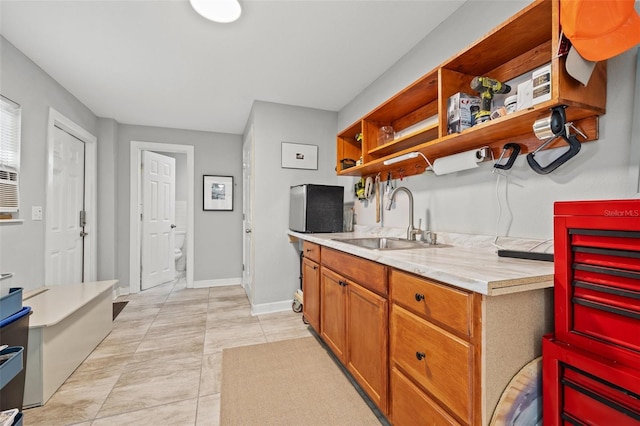 kitchen with baseboards, open shelves, a sink, light countertops, and brown cabinets