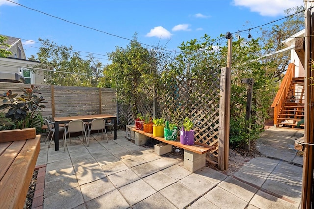 view of patio with outdoor dining area, stairs, and fence