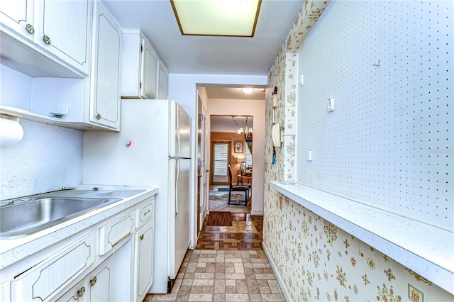 kitchen featuring stone finish flooring, white cabinetry, freestanding refrigerator, light countertops, and a chandelier