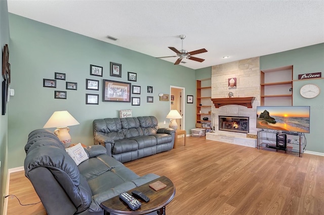 living area with a ceiling fan, visible vents, baseboards, a stone fireplace, and light wood-style floors