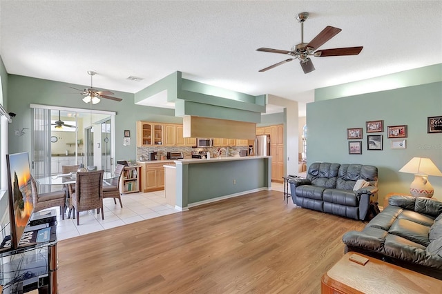 living area featuring visible vents, a textured ceiling, ceiling fan, and light wood finished floors