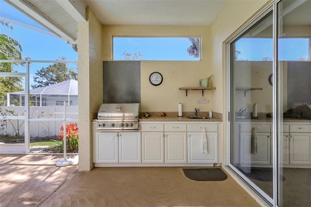 view of patio featuring glass enclosure, fence, exterior kitchen, area for grilling, and a sink