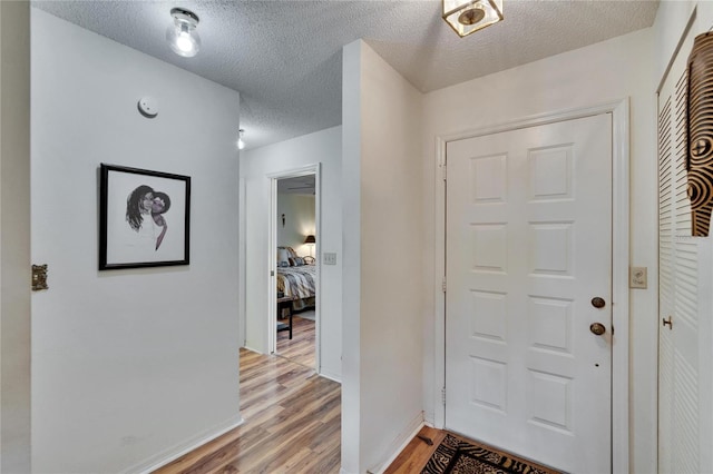 foyer entrance with baseboards, light wood-type flooring, and a textured ceiling