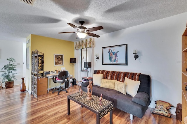 living room featuring visible vents, a textured ceiling, ceiling fan, and light wood finished floors