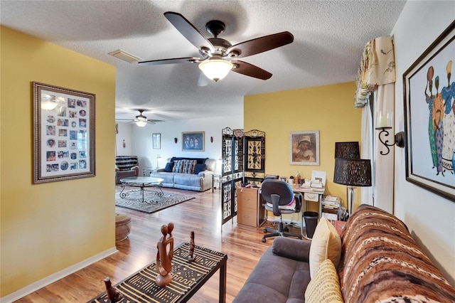 living area featuring light wood finished floors, visible vents, ceiling fan, baseboards, and a textured ceiling