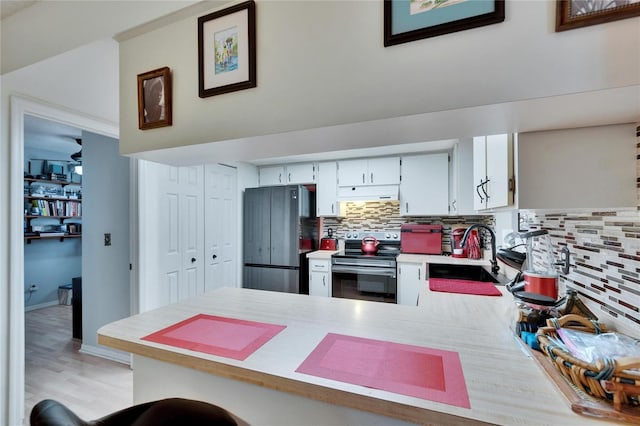 kitchen with a peninsula, stainless steel electric stove, freestanding refrigerator, a sink, and under cabinet range hood