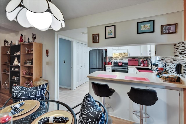 kitchen featuring tasteful backsplash, stainless steel electric range oven, freestanding refrigerator, white cabinetry, and a sink