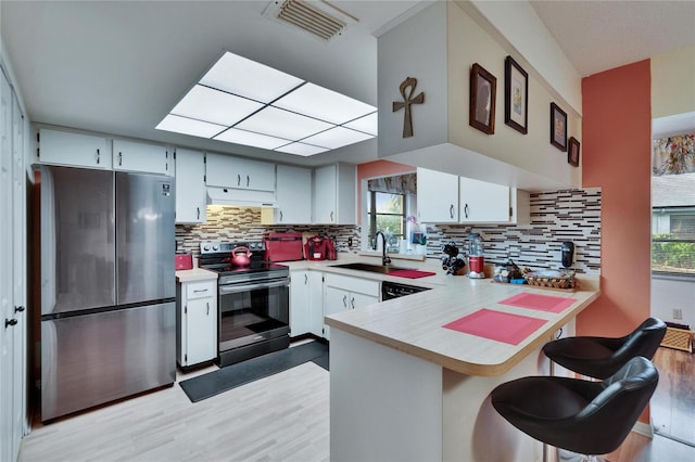 kitchen with visible vents, under cabinet range hood, a sink, stainless steel appliances, and a peninsula