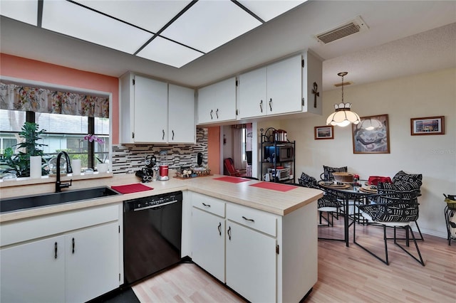 kitchen featuring visible vents, backsplash, dishwasher, a peninsula, and a sink