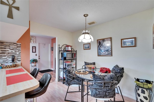 dining area with visible vents, baseboards, light wood-style floors, and a textured ceiling