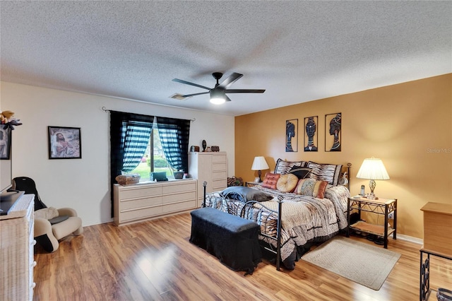 bedroom featuring a textured ceiling, light wood-style floors, visible vents, and ceiling fan