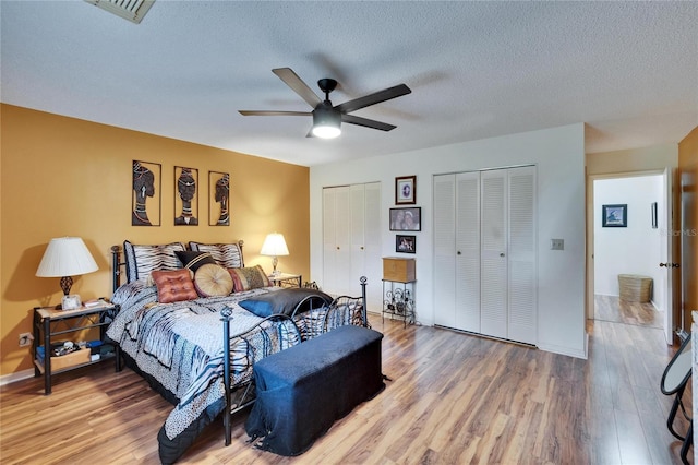 bedroom with visible vents, multiple closets, light wood-style flooring, a ceiling fan, and a textured ceiling