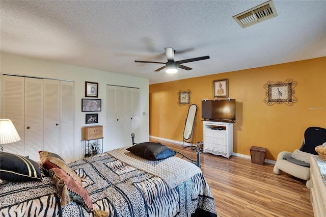 bedroom featuring visible vents, multiple closets, a textured ceiling, light wood finished floors, and baseboards