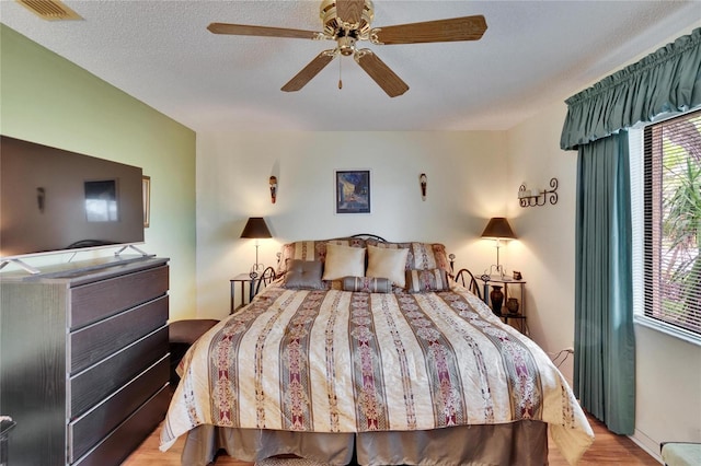 bedroom with visible vents, a textured ceiling, wood finished floors, and a ceiling fan