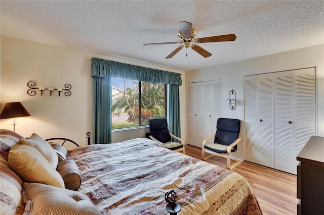 bedroom with a textured ceiling, two closets, ceiling fan, and light wood finished floors