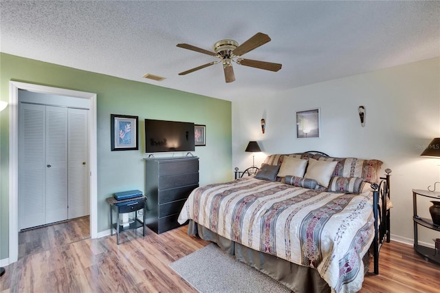 bedroom featuring baseboards, wood finished floors, visible vents, and a textured ceiling