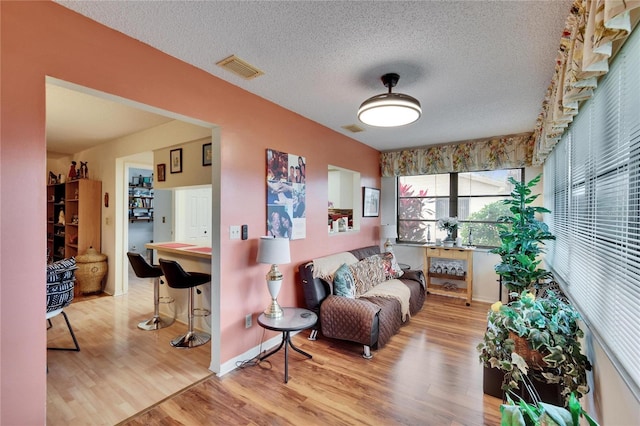 sitting room with baseboards, wood finished floors, visible vents, and a textured ceiling