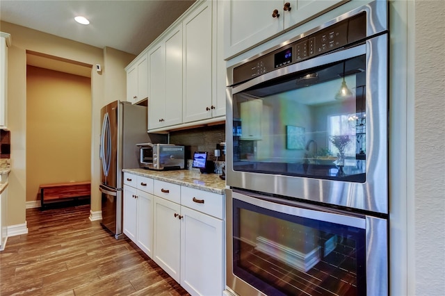 kitchen with wood finished floors, light stone countertops, decorative backsplash, white cabinets, and double oven