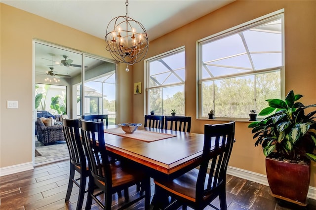 dining space with ceiling fan with notable chandelier, baseboards, and dark wood-style flooring