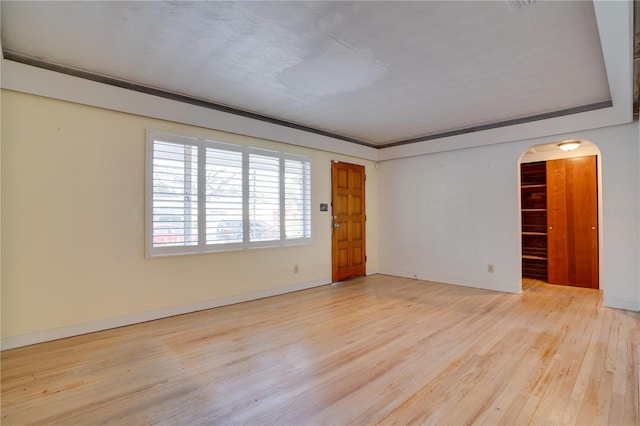 empty room with baseboards, arched walkways, and light wood finished floors