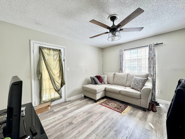 living area with ceiling fan, baseboards, light wood finished floors, and a textured ceiling