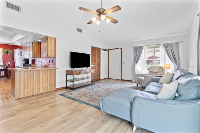 living room with lofted ceiling, light wood-style flooring, a ceiling fan, and visible vents