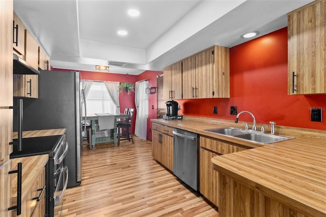 kitchen with extractor fan, butcher block counters, appliances with stainless steel finishes, light wood-style floors, and a sink