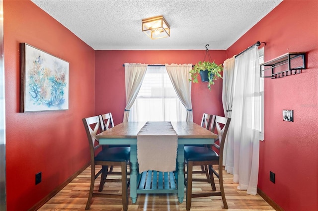 dining space with a textured ceiling, baseboards, and wood finished floors