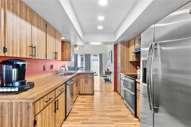 kitchen featuring under cabinet range hood, light wood-style flooring, a peninsula, stainless steel appliances, and a sink