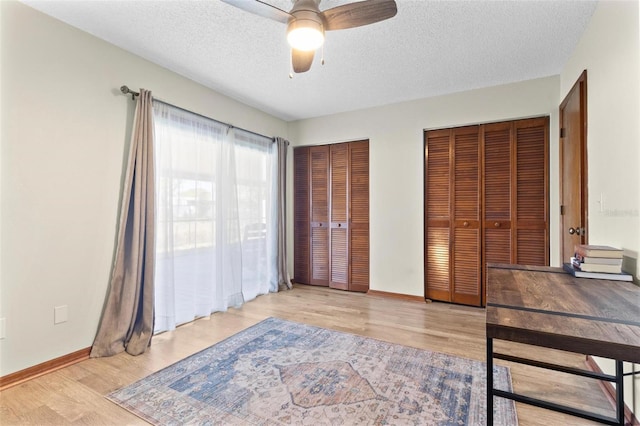 unfurnished bedroom with baseboards, multiple closets, a textured ceiling, and wood finished floors