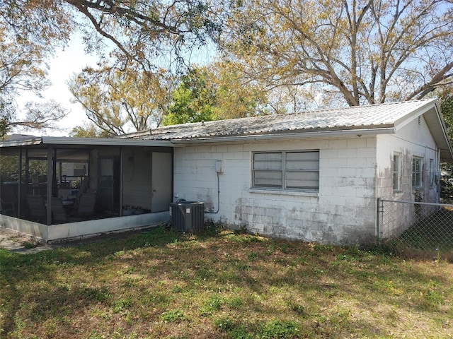 view of side of home with concrete block siding, fence, a yard, a sunroom, and metal roof