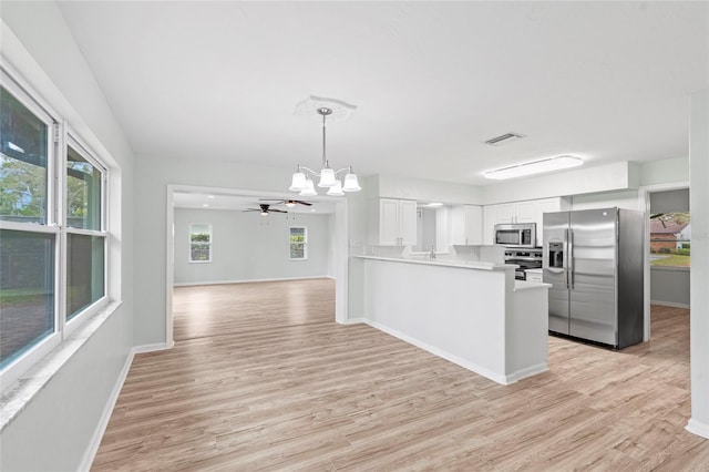 kitchen with light wood-type flooring, stainless steel appliances, white cabinets, baseboards, and hanging light fixtures