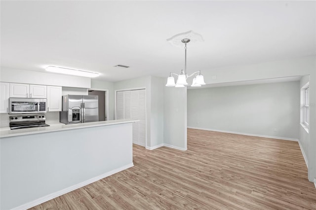 kitchen with light countertops, light wood-style floors, appliances with stainless steel finishes, white cabinetry, and a notable chandelier