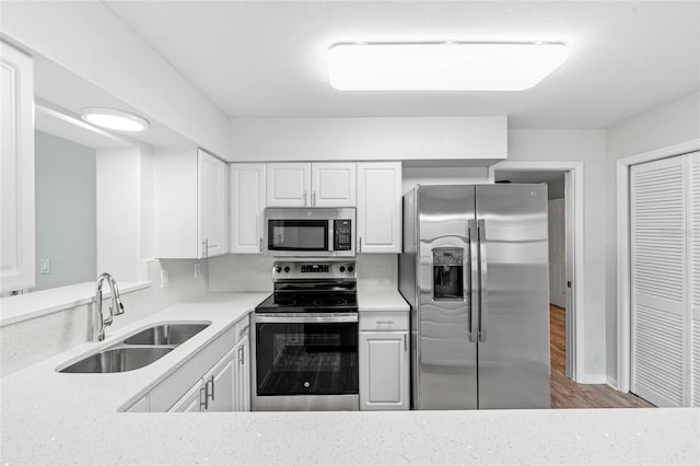 kitchen featuring light stone countertops, appliances with stainless steel finishes, wood finished floors, white cabinets, and a sink